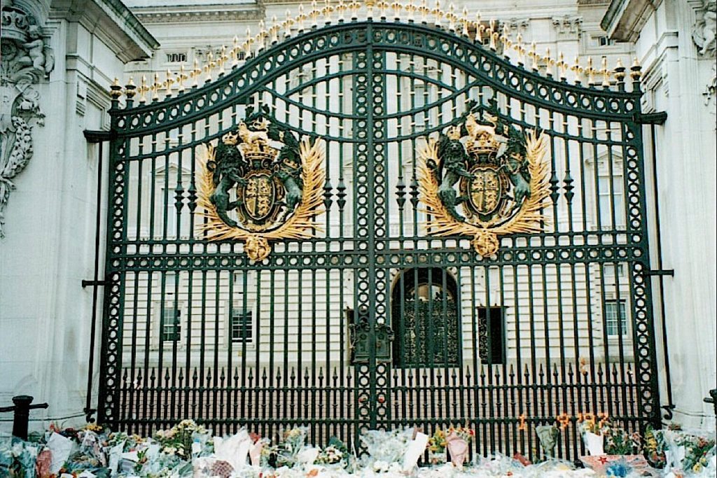 Image shows the decorative gates to Buckingham Palace. In the foreground are a number of bunches of flowers.