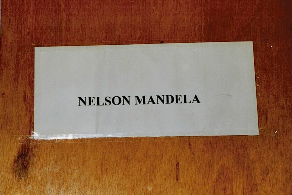 Image shows the name Nelson Mandela on a prison cell wall