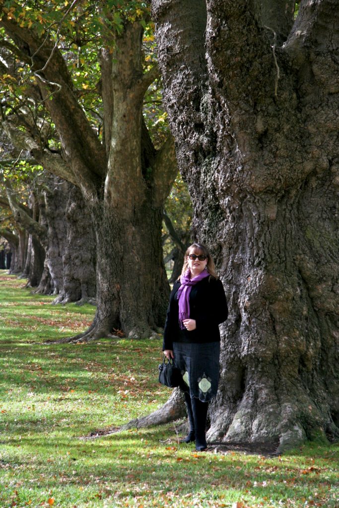 Mardi in foreground in black dress and pink scarf stanging in front of tree.  Behinf her off at an angle are several other trees in line