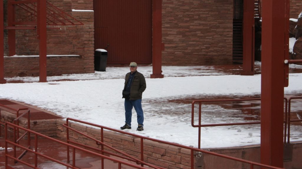 Image taken from a distance of me, standing on the centre of the stage at Red Rocks. The stage is covered in snow.