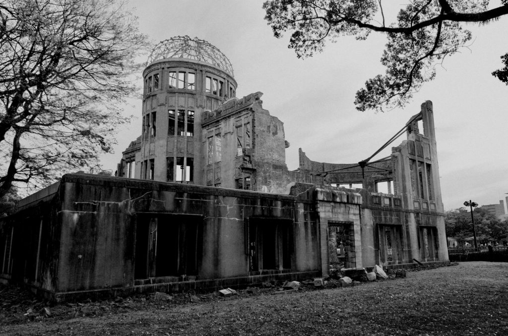Black and white image of the peace dome in Hiroshima. Trees bound the image which shows the damaged dome and structures.