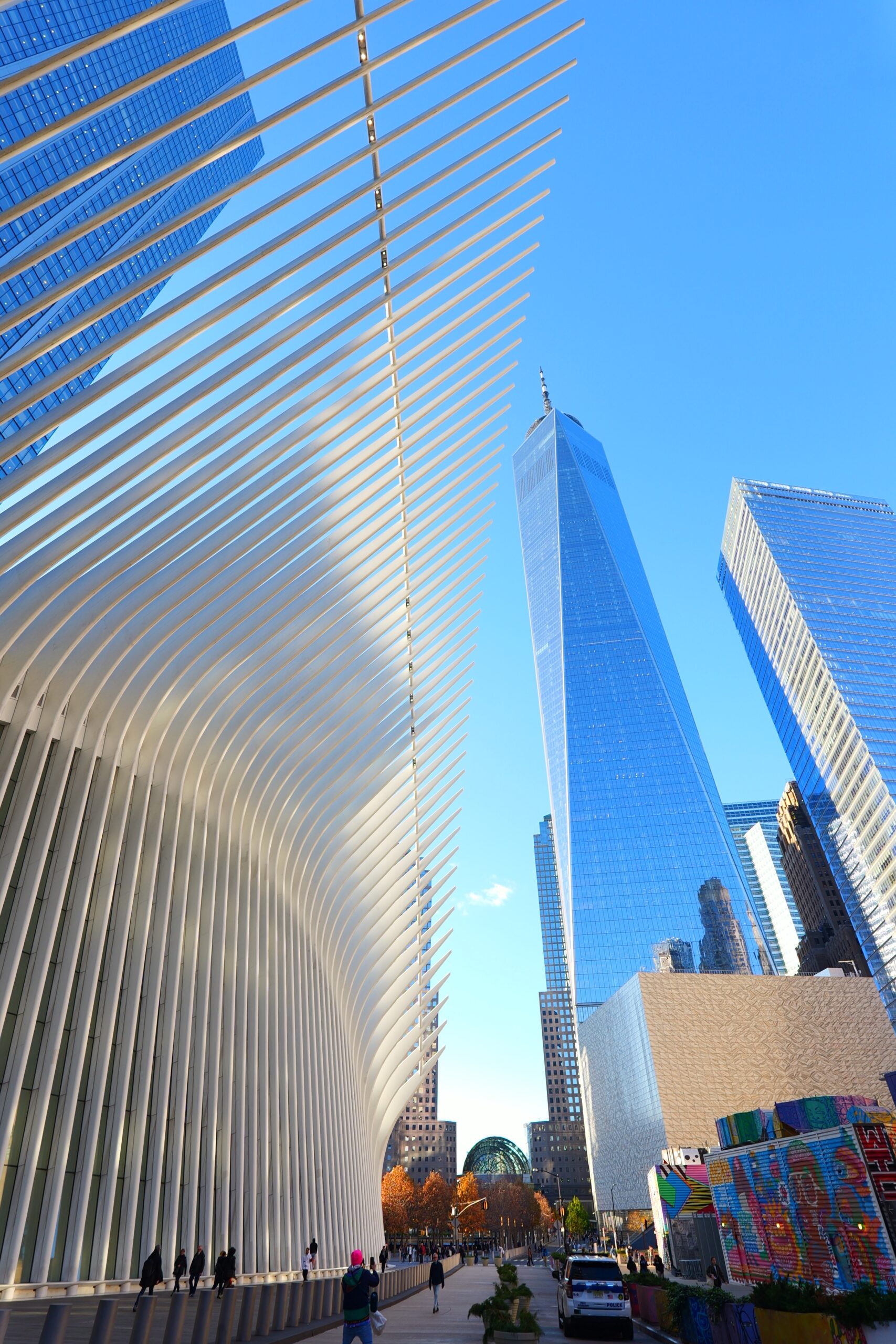 Image of the WTC. Blue sky, blue glass building. It’s really tall. Oculus in foreground left, it’s white