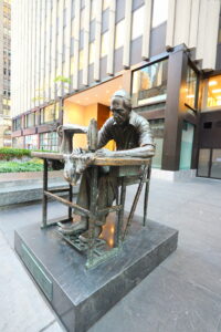 A sculpture of a man sewing on a sewing machine