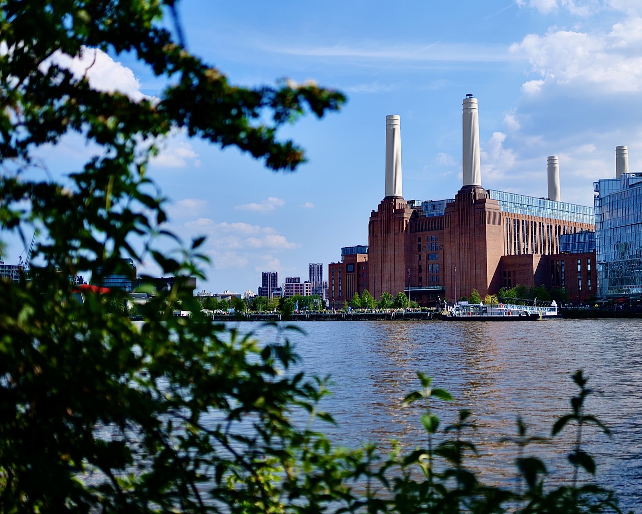 animate from across the Thames of the power station. the river thames looks blue and branches and leaves are in the foreground framing the power station