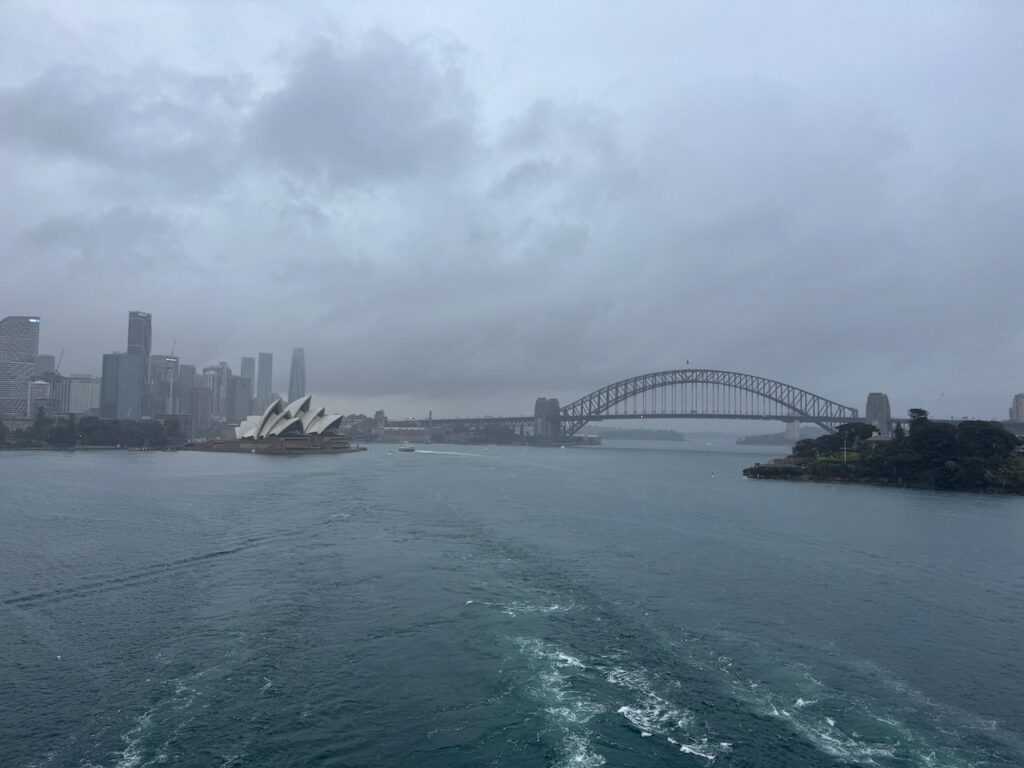 An image of Sydney Harbour the Opera house and Harbour Bridge and City in interview view. He's very very cloudy and overcast and rainy.