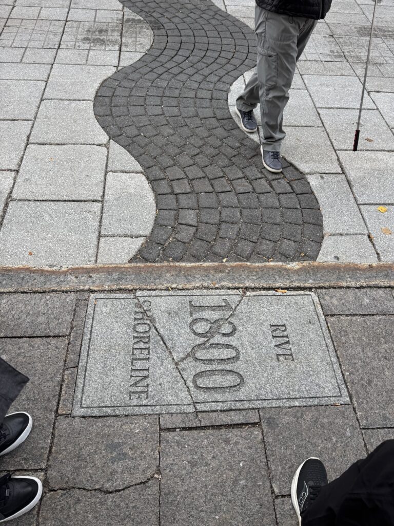 A cobbled toad showing the numbers 1800. The road has a wavy line of black stones surrounded by white. The wave represents the river bank in 1800.