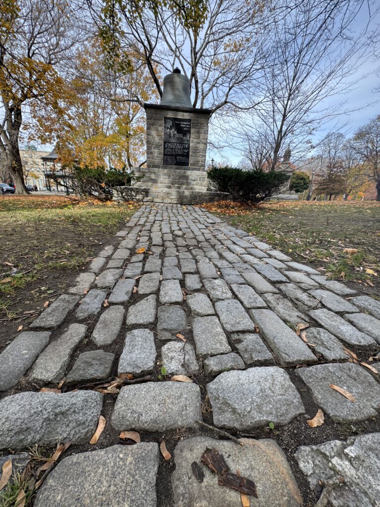 A cobbled pathway leads to a statue. Statue is a bill sitting on a paying respect to the emergency services.