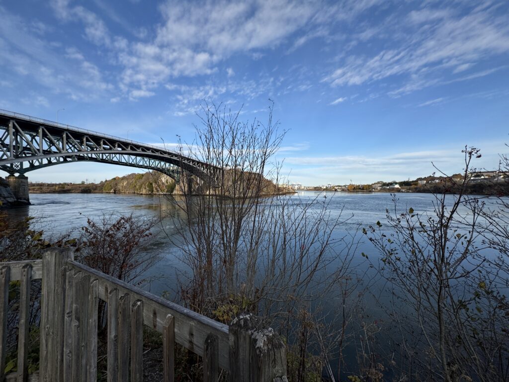 And Major the bridge crossing the river at the reversing rapids the river stretches out left and light. The sky is blue and it’s a sunny day.
